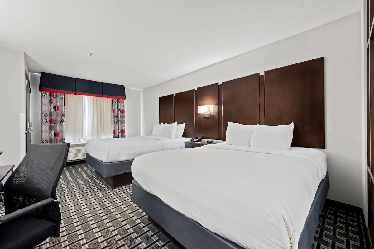 Habitación de hotel con dos camas, un escritorio, una silla y una alfombra estampada.