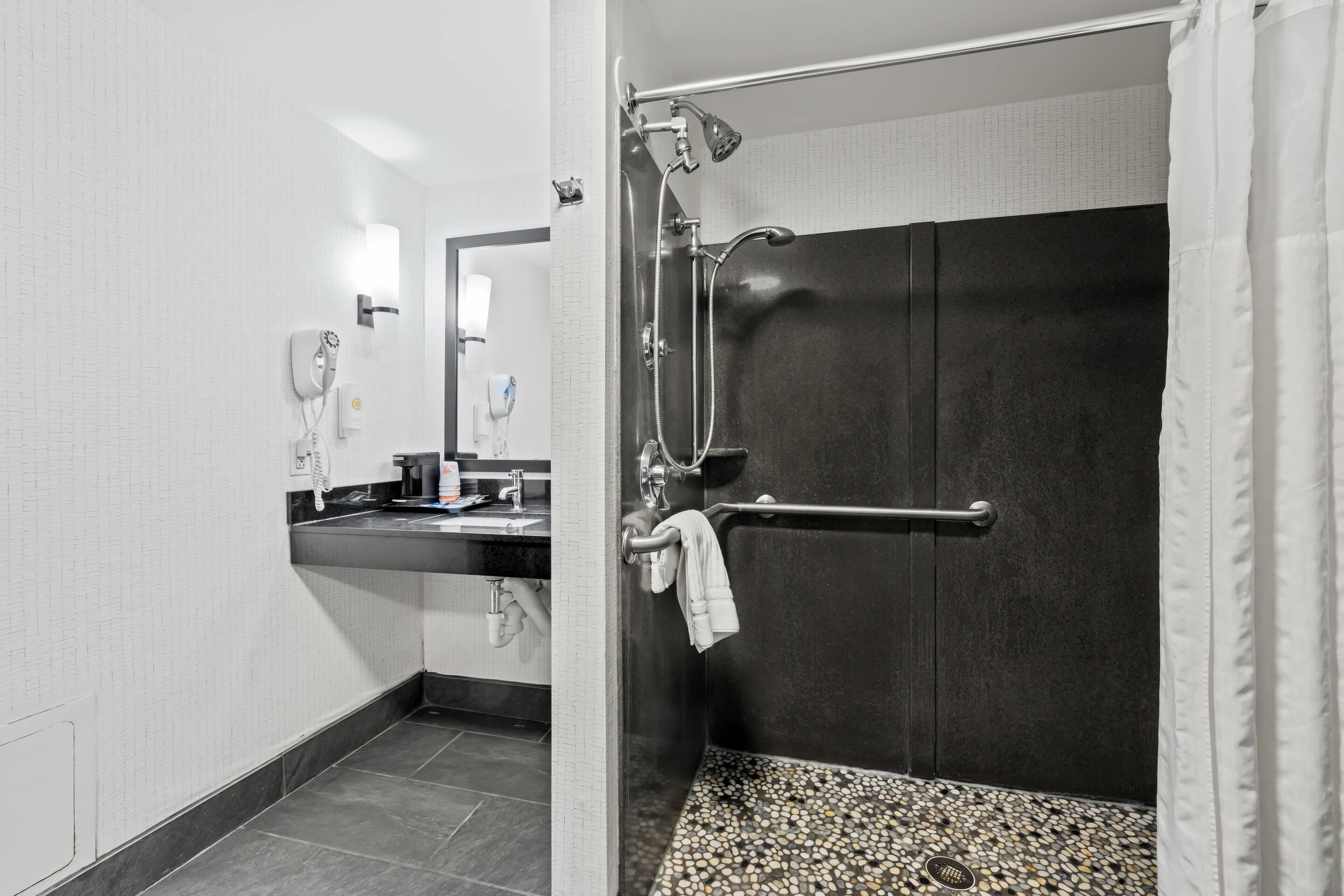 A modern bathroom with a shower, a towel rack, a sink with a mirror, and a telephone.