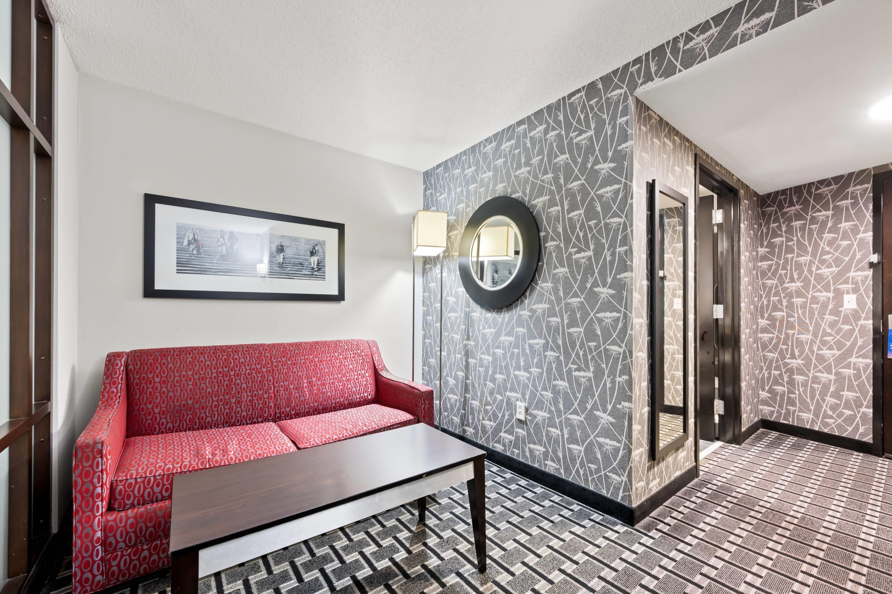 A modern lobby with a patterned floor, a red sofa, a coffee table, a framed picture, and a wall-mounted mirror.