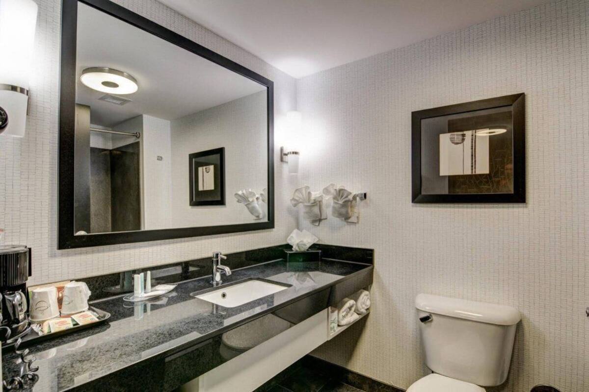 Un baño moderno con un espejo grande, un lavamanos, un inodoro y un perchero para toallas.