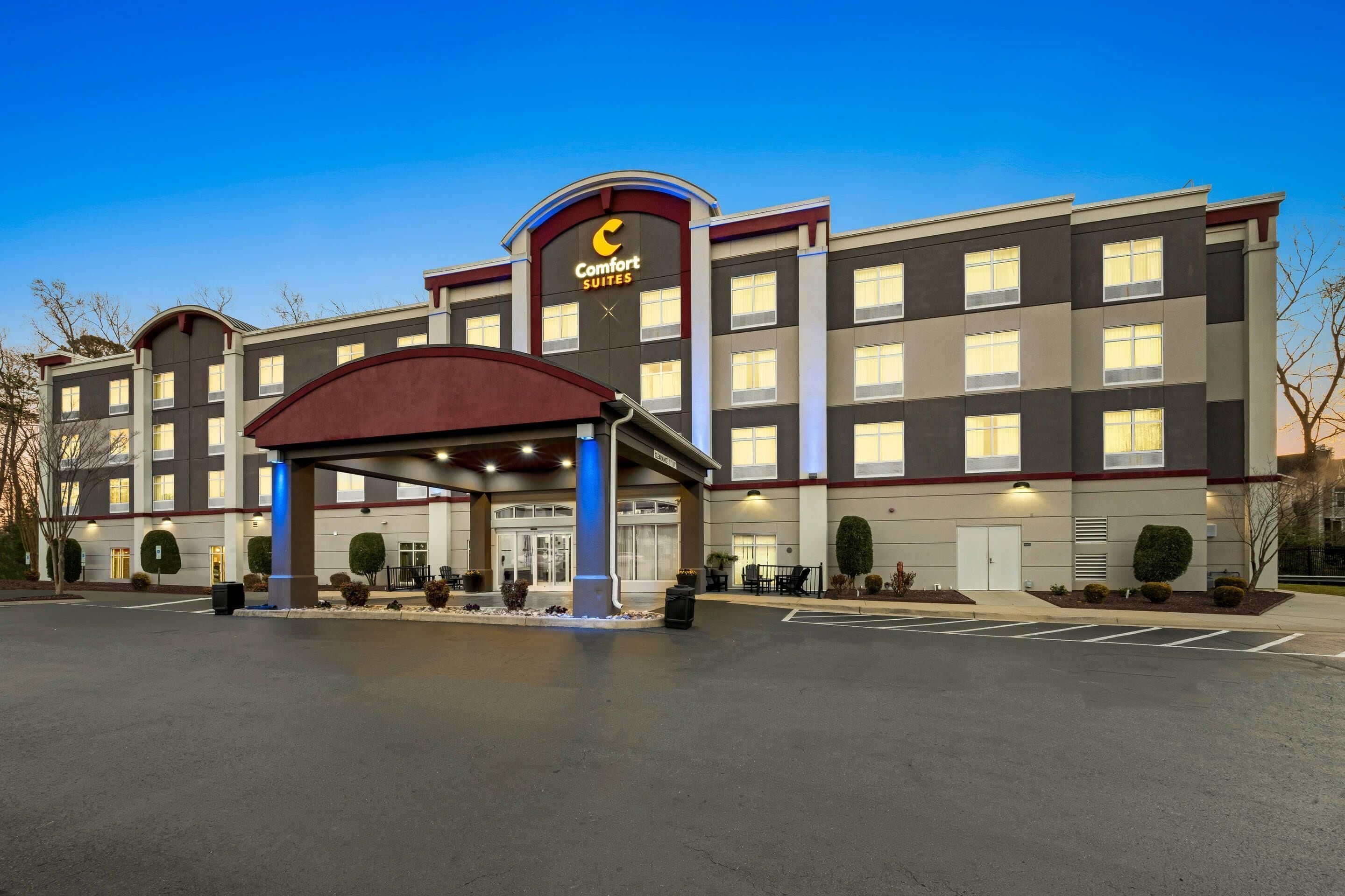 Un hotel con un llamativo letrero de 'Comfort Suites', un acceso cubierto y un estacionamiento.