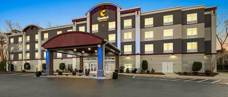 Un hotel con un llamativo letrero de 'Comfort Suites', un acceso cubierto y un estacionamiento.