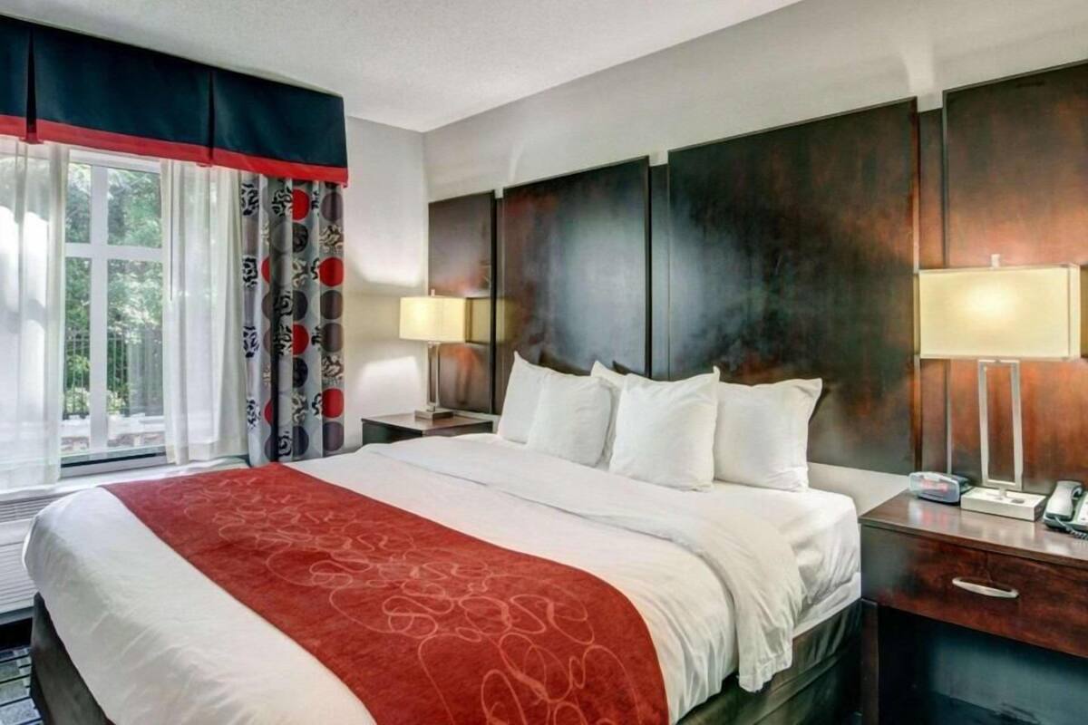 Habitación de hotel con una cama grande, dos mesitas de noche, un buró, una ventana con cortinas y una lámpara fijada a la pared.
