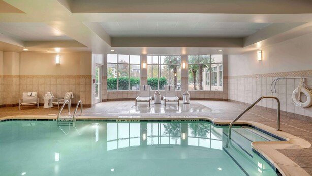 A swimming pool with lounge chairs and sun loungers, a lifebuoy, and a view of greenery outside. - Hilton Garden Inn Charlotte/Concord (Concord)