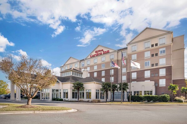 A Hilton Garden Inn with a modern design, featuring a prominent entrance, multiple floors, and a clear sky.