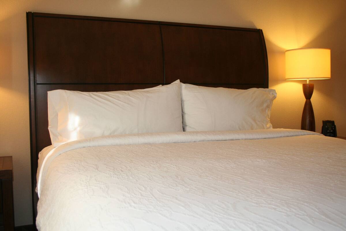 A hotel room with a large bed, a wooden headboard, and a bedside lamp.