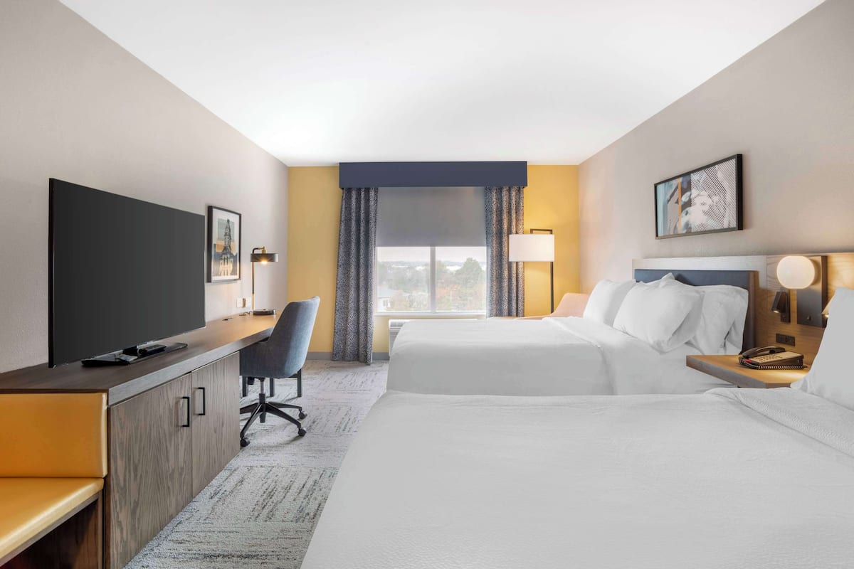A hotel room with a bed, a desk, a chair, a TV, and a window with curtains.