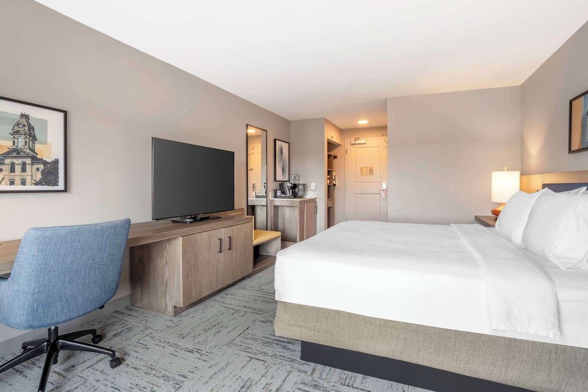 A hotel room with a bed, desk, chair, television, and a framed picture on the wall.