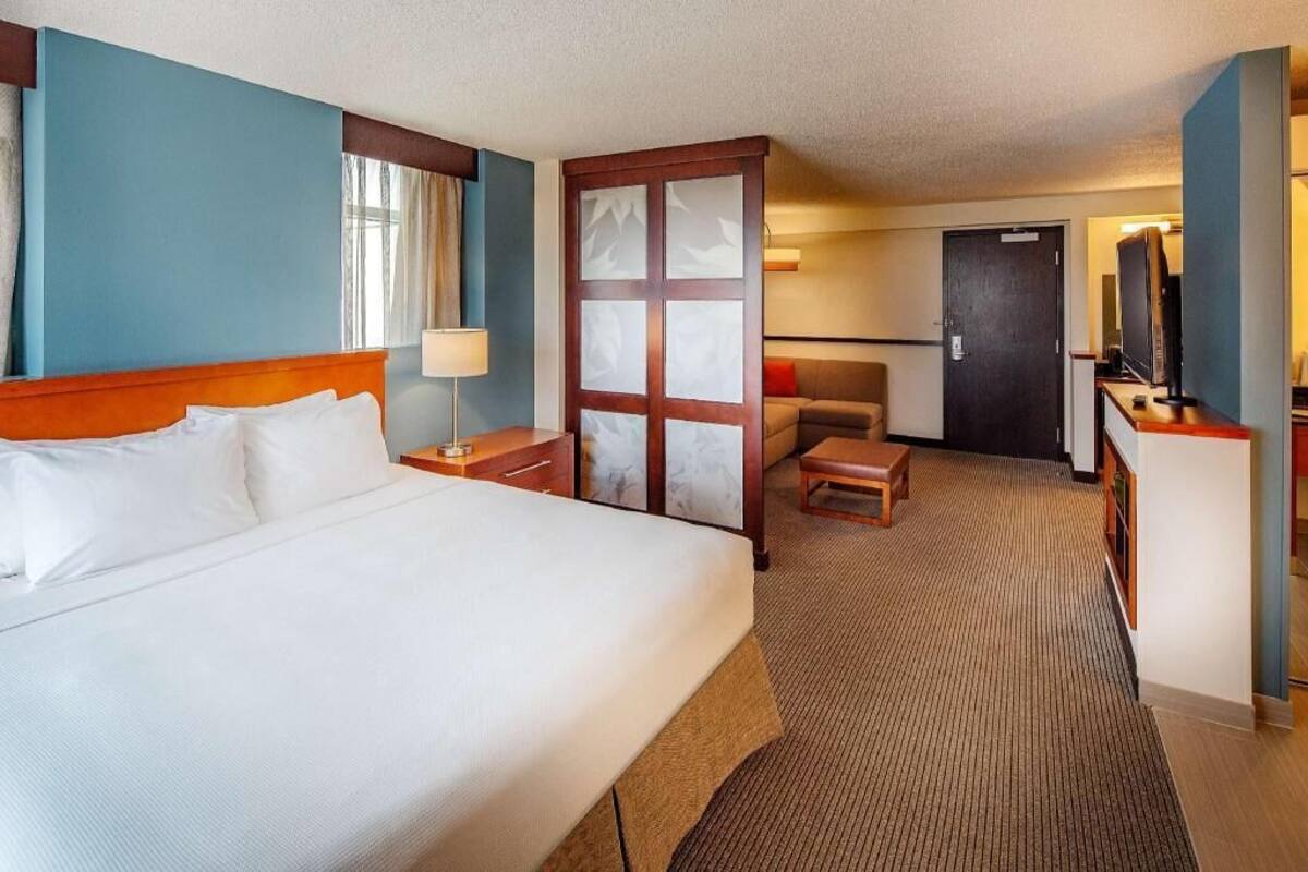 A hotel room with a bed, a desk, a chair, a television, and a door.