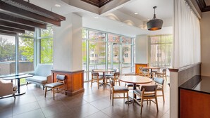 Un espace repas moderne avec des tables et des chaises rondes, de grandes fenêtres et une vue sur les bâtiments environnants.