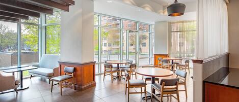 A modern dining area with round tables and chairs, large windows, and a view of buildings outside.