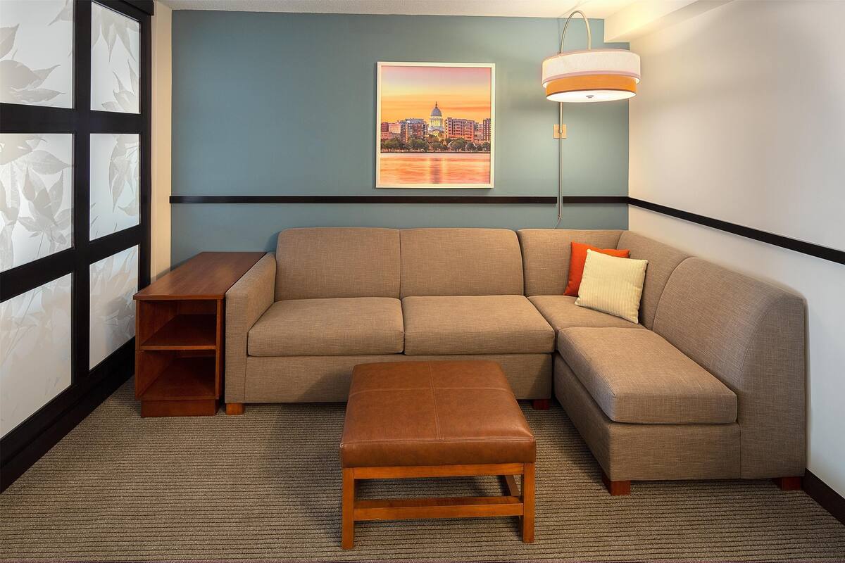 A living room with a sectional sofa, a wooden bench, a side table, and a cityscape painting on the wall.