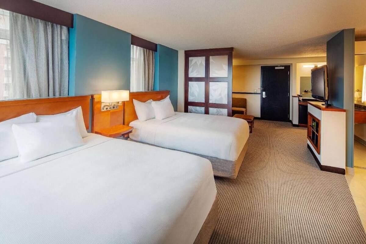 A hotel room with two beds, a desk, a television, and a door leading to a bathroom.