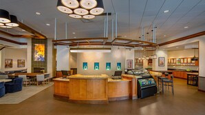 Un hall d’hôtel moderne avec un comptoir d’accueil central, un espace salon et un bar.