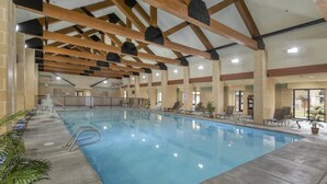 Una piscina interior con suelo de baldosas, vigas de madera y sillones de descanso a lo largo de los bordes.