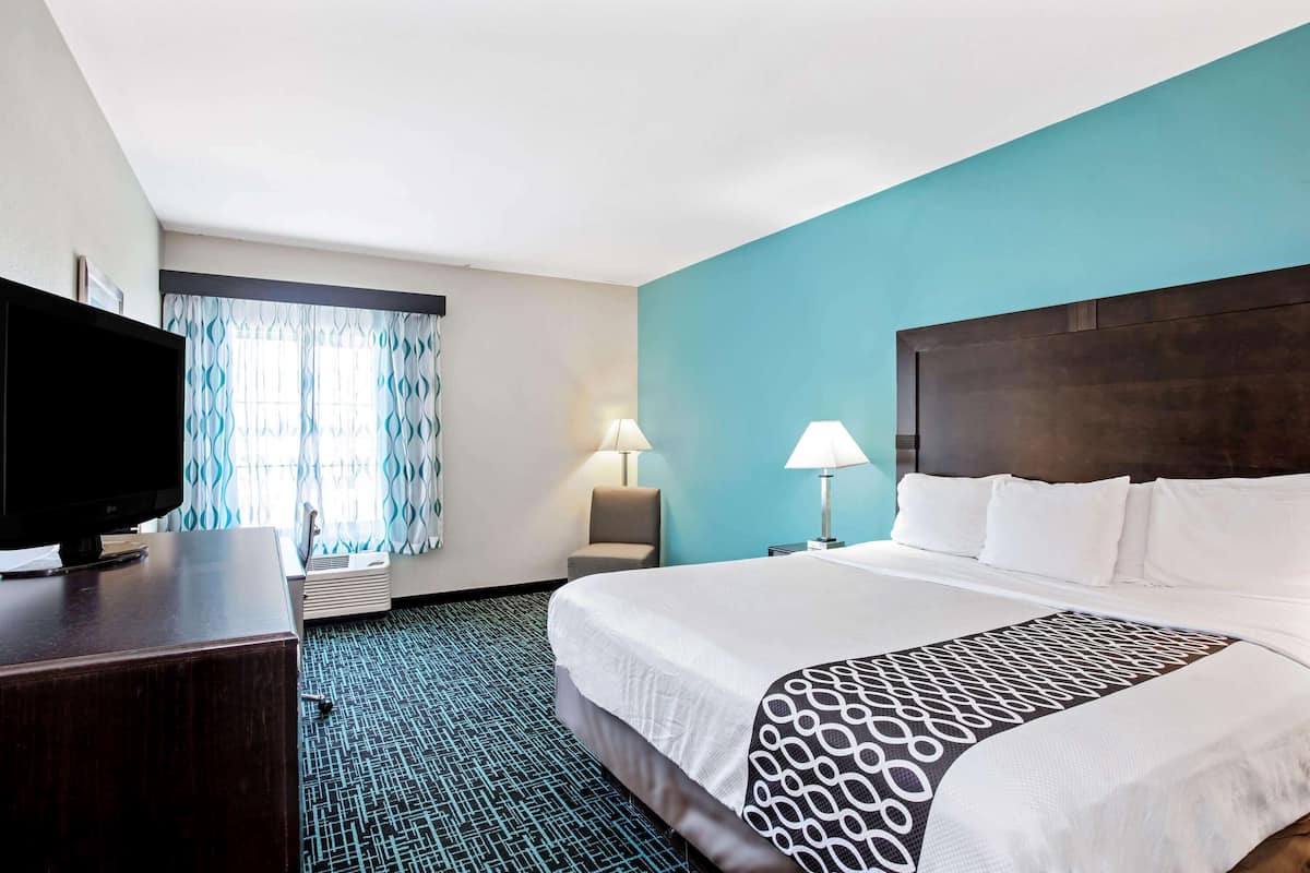 Une chambre d’hôtel avec un lit, un bureau avec une télévision, une lampe et une fenêtre avec des rideaux.