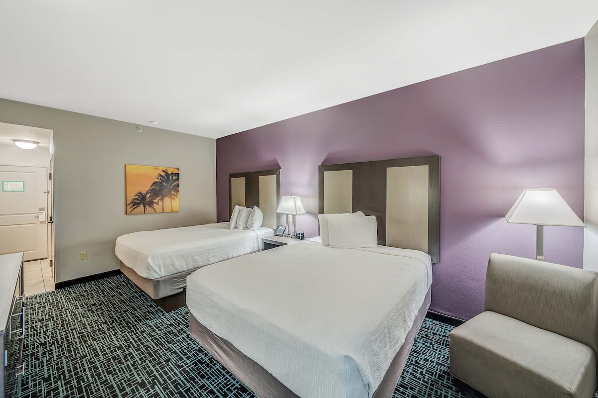 Une chambre d’hôtel avec deux lits, un bureau, une chaise, un tableau et une lampe.