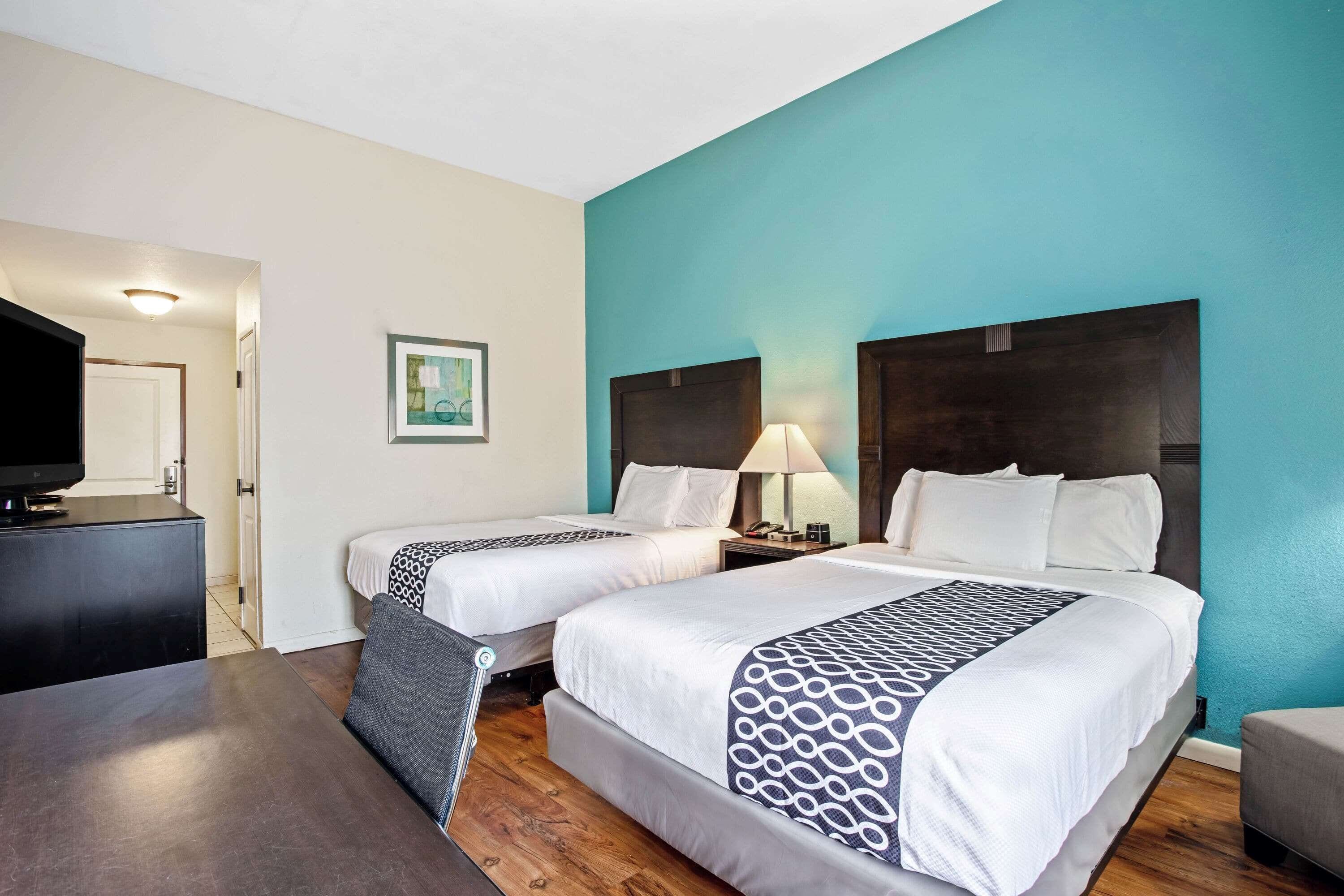 A hotel room with two beds, a desk, a TV, and a painting on the wall.