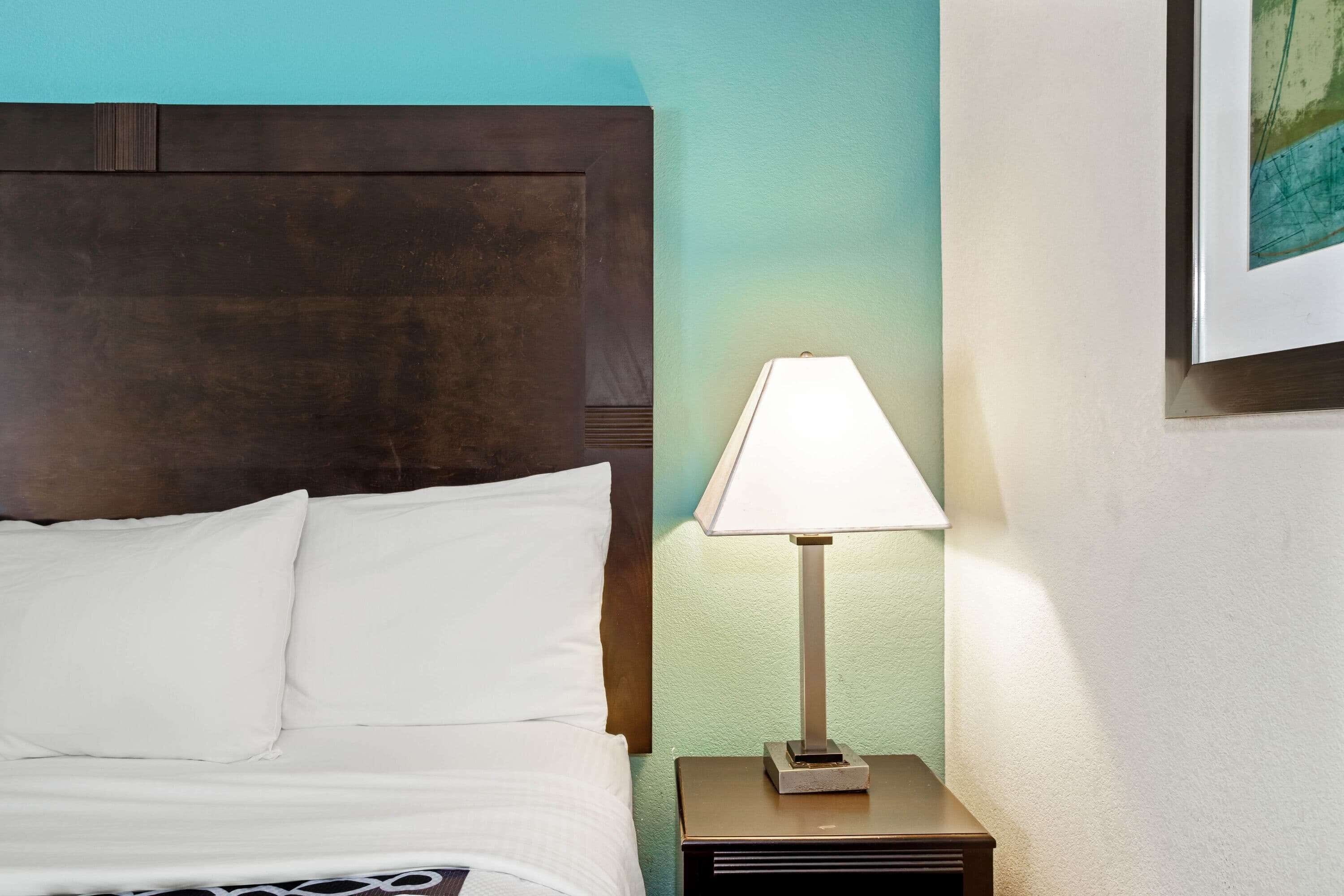 A neatly made bed with white linens, a dark wooden headboard, and a bedside table with a lamp.