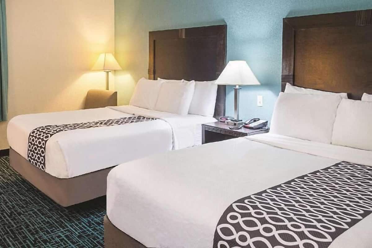 A hotel room with two beds, a nightstand with a lamp, and a wall-mounted phone.