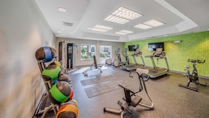 Un gimnasio con equipamiento de ejercicio, un ventanal grande y una pared verde.