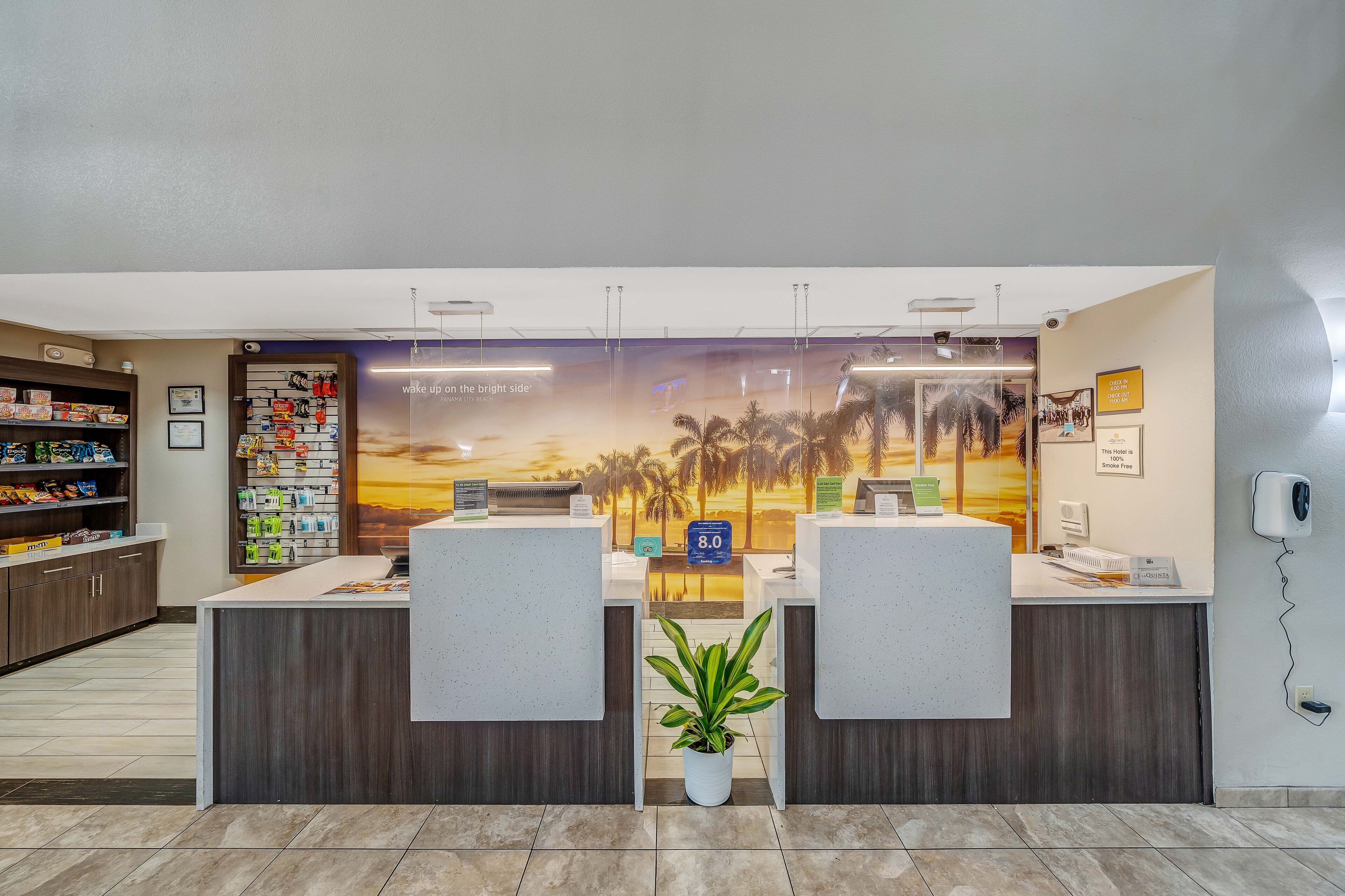 A hotel reception area with a reception desk, a plant, and a mural of palm trees.
