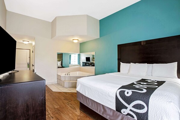 A hotel room with a bed, a TV, a bathroom with a bathtub, and a mirror.