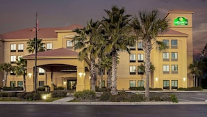 Un hotel con fachada amarilla, palmeras y un cartel que dice 'La Quinta Inn & Suites'.