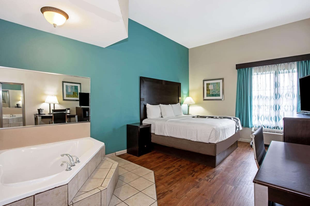 Une chambre d’hôtel avec une grande baignoire, deux lits, un bureau et une fenêtre avec des rideaux.