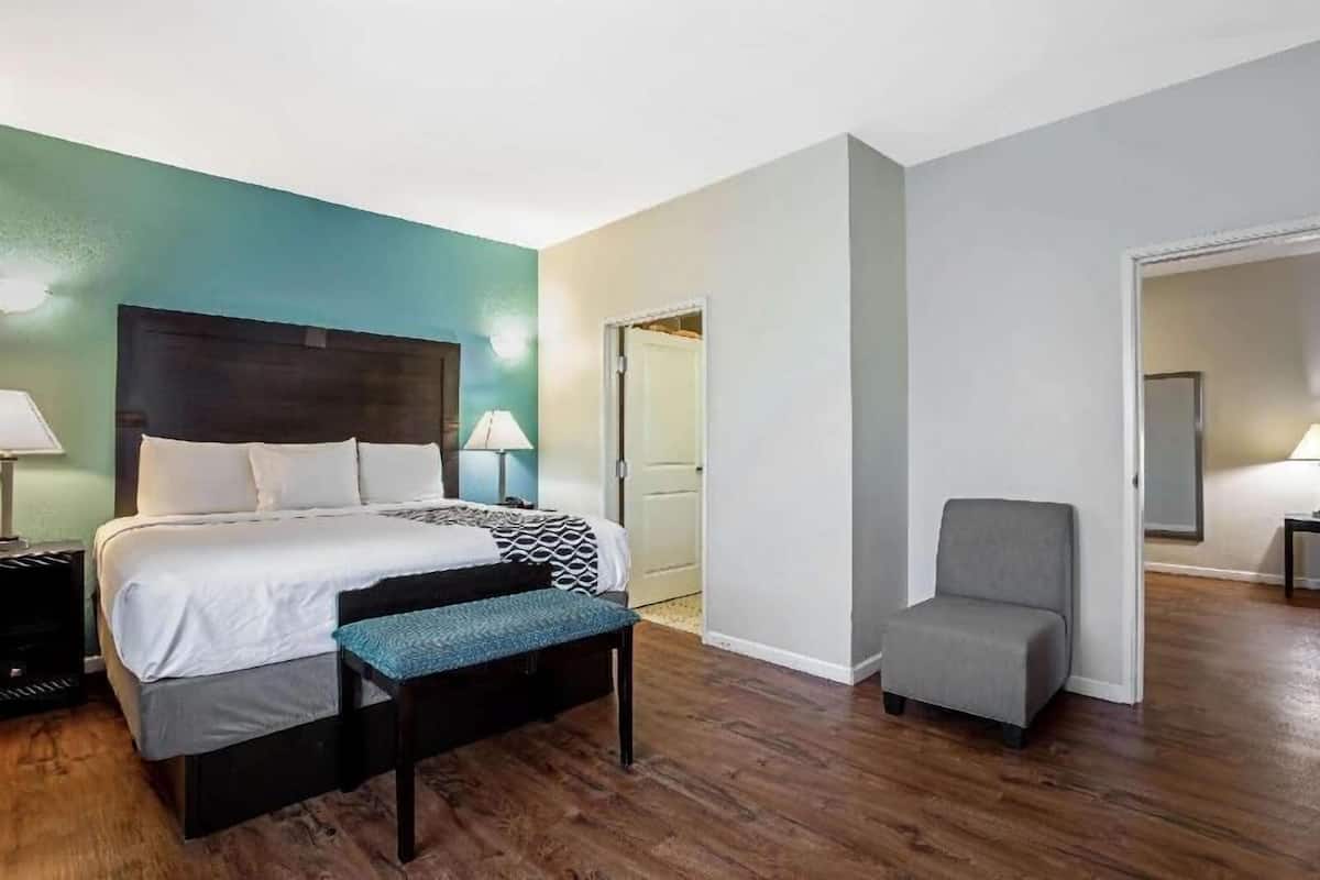 Une chambre d’hôtel comprenant un lit, une table de chevet, une lampe, une chaise et une porte donnant sur une autre pièce.