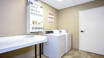 A laundry area with a sink, a washing machine, and a dryer. There are signs for soap, bleach, and softeners.