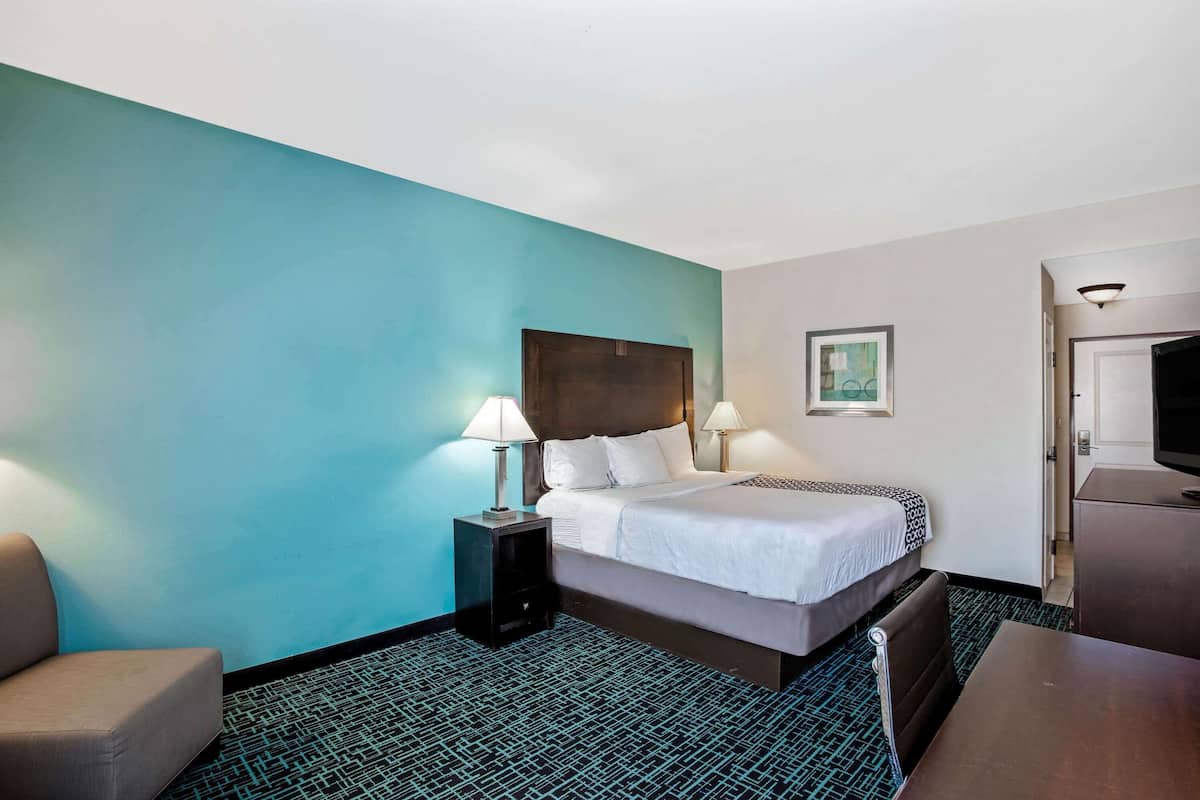 Une chambre d’hôtel comprenant un lit, deux tables de chevet avec des lampes, une chaise, un bureau et un téléviseur.
