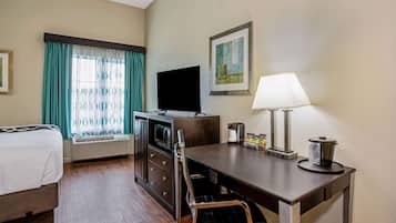 Habitación de hotel con cama, escritorio con lámpara, televisor, microondas y cafetera.