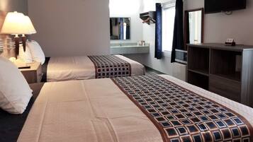 A hotel room with two beds, a bedside table with a lamp, a mirror, a TV, and a wardrobe.