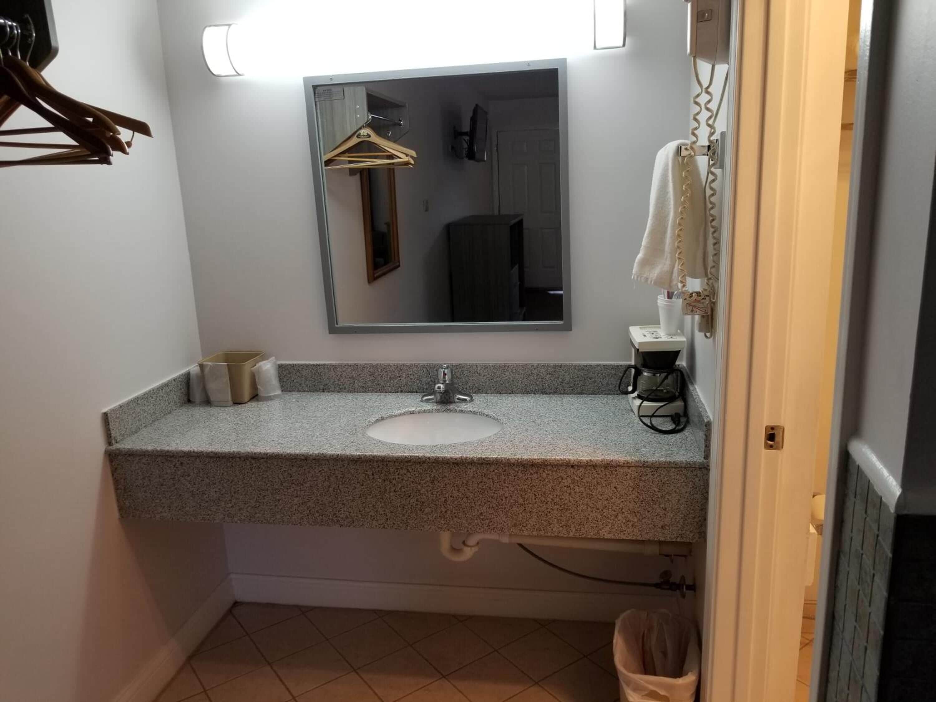 Une salle de bain avec un comptoir en granit, un lavabo, un miroir, un porte-serviettes et une poubelle.