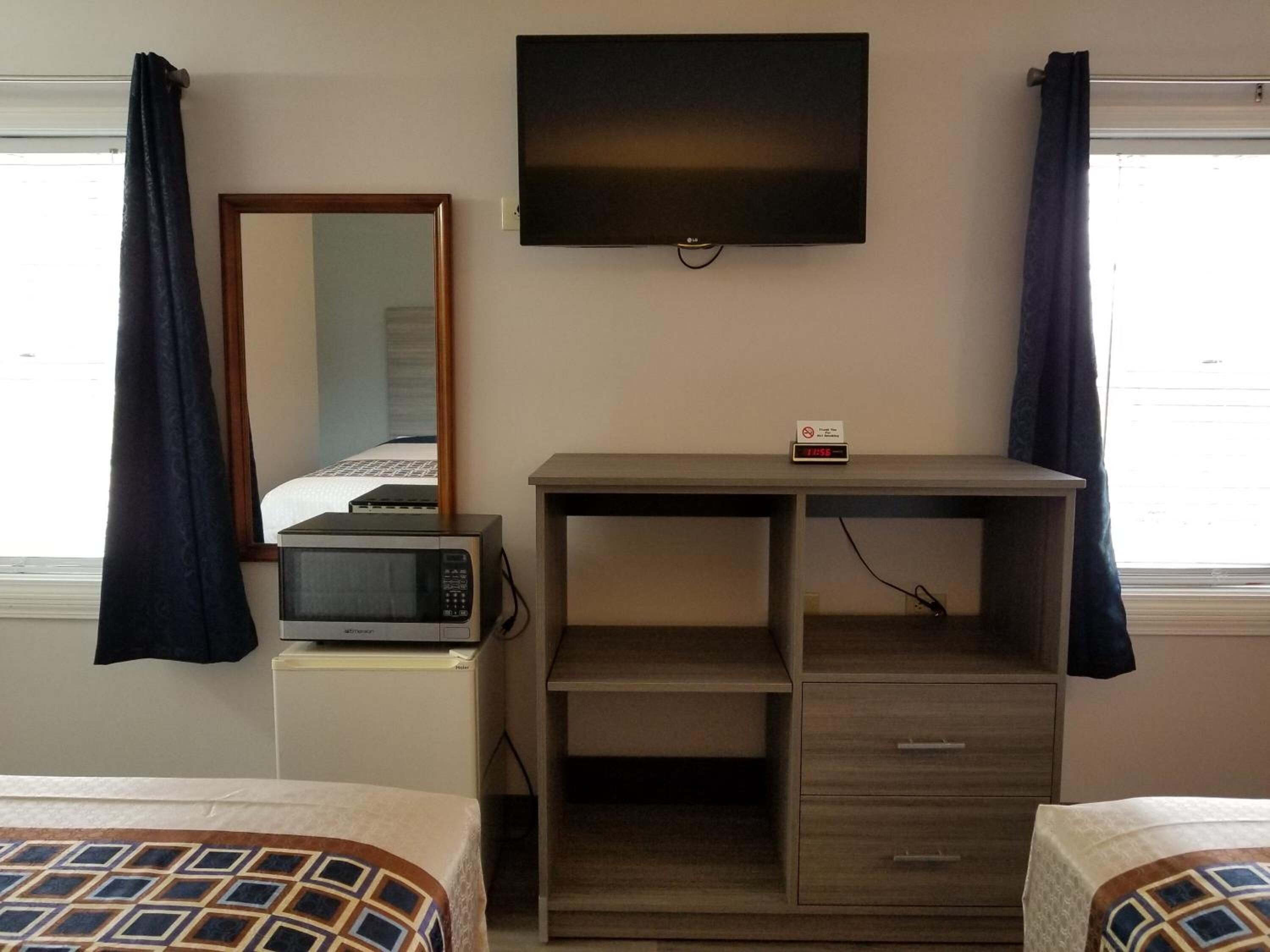 A hotel room with a bed, a desk with a microwave, a TV, and a clock.