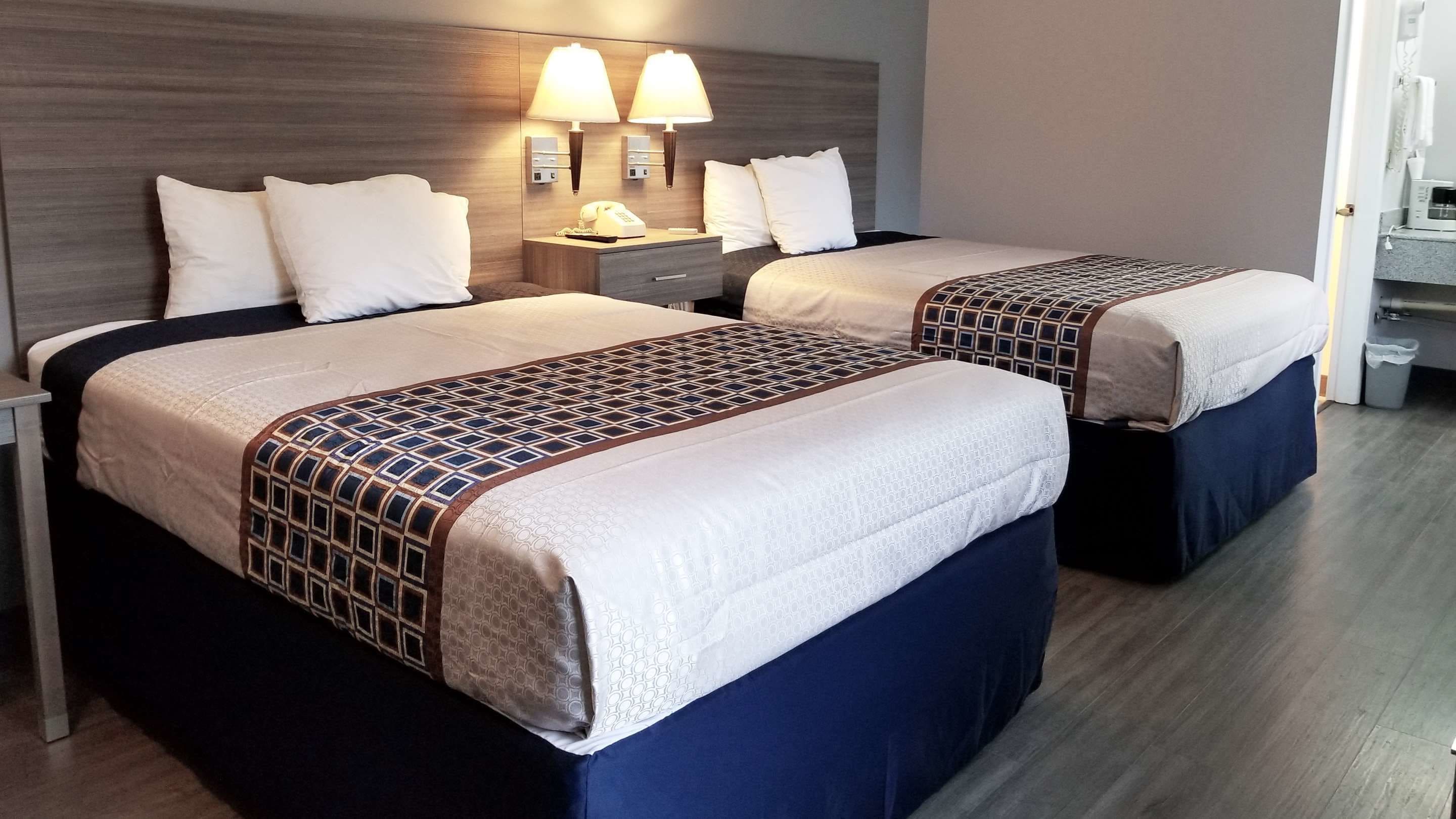 A hotel room with two beds, each with a patterned bedspread and pillows. There are bedside lamps and a nightstand with a phone.