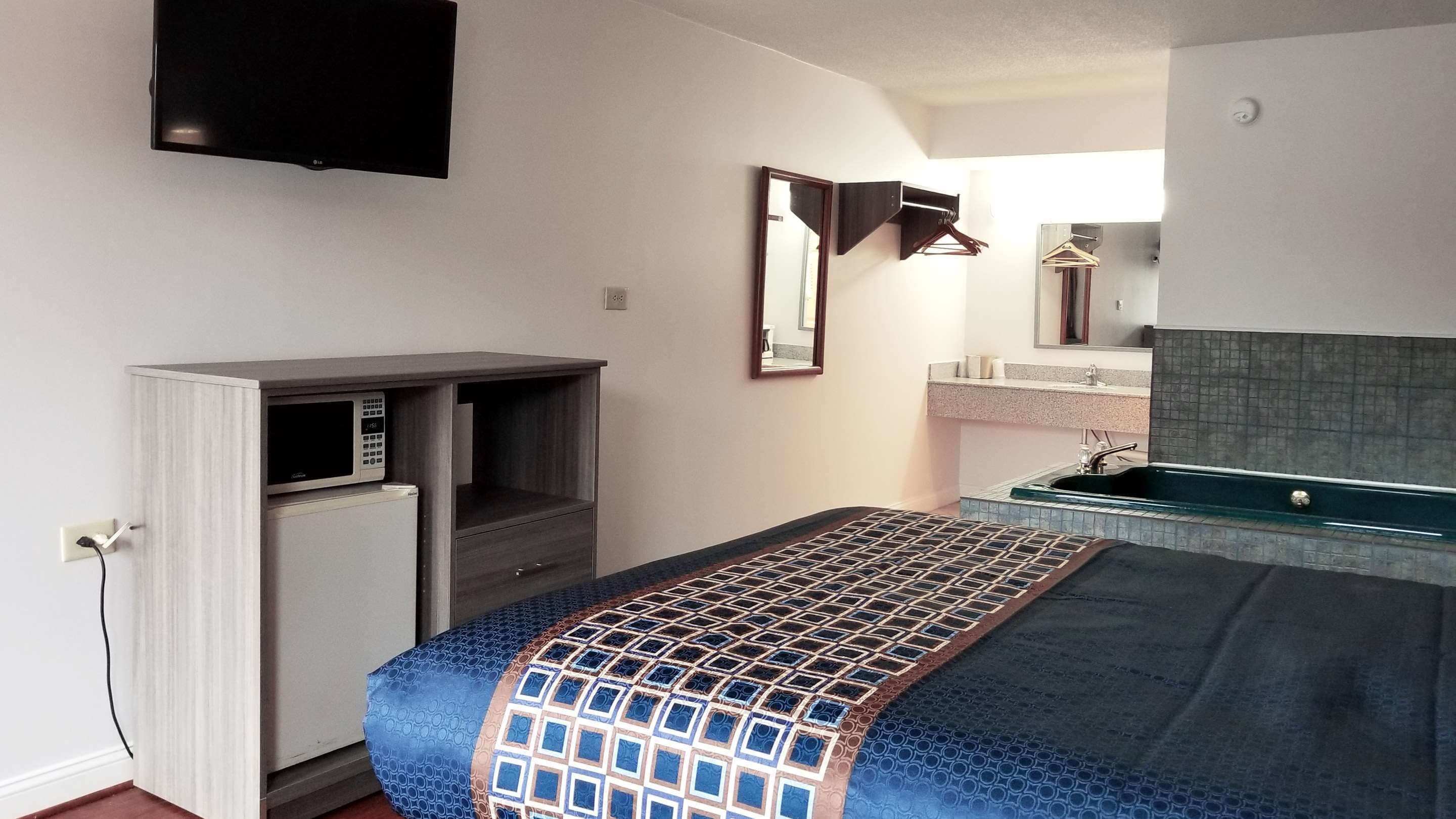 Habitación de hotel compacta con cama, televisión integrada, kitchenette pequeña y baño con espejo y lavamanos.