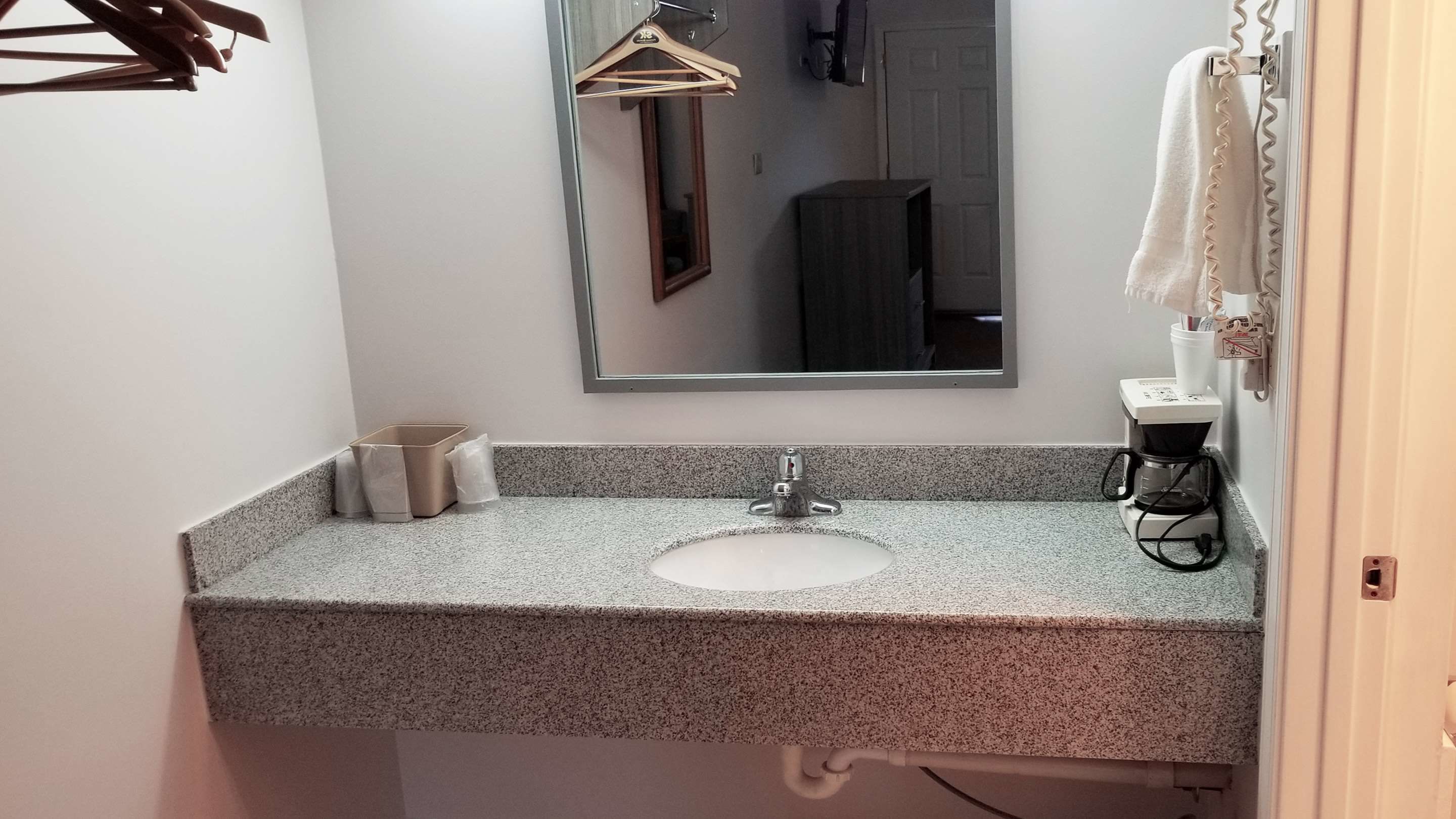 A bathroom with a granite countertop sink, a mirror, a towel rack, and a coffee maker.