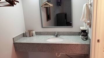 A bathroom with a granite countertop sink, a mirror, a towel rack, and a coffee maker.