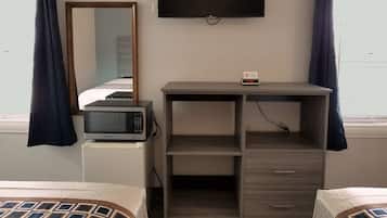 A hotel room with a bed, a microwave on a small white appliance, a TV on the wall, and a clock displaying 11:56.