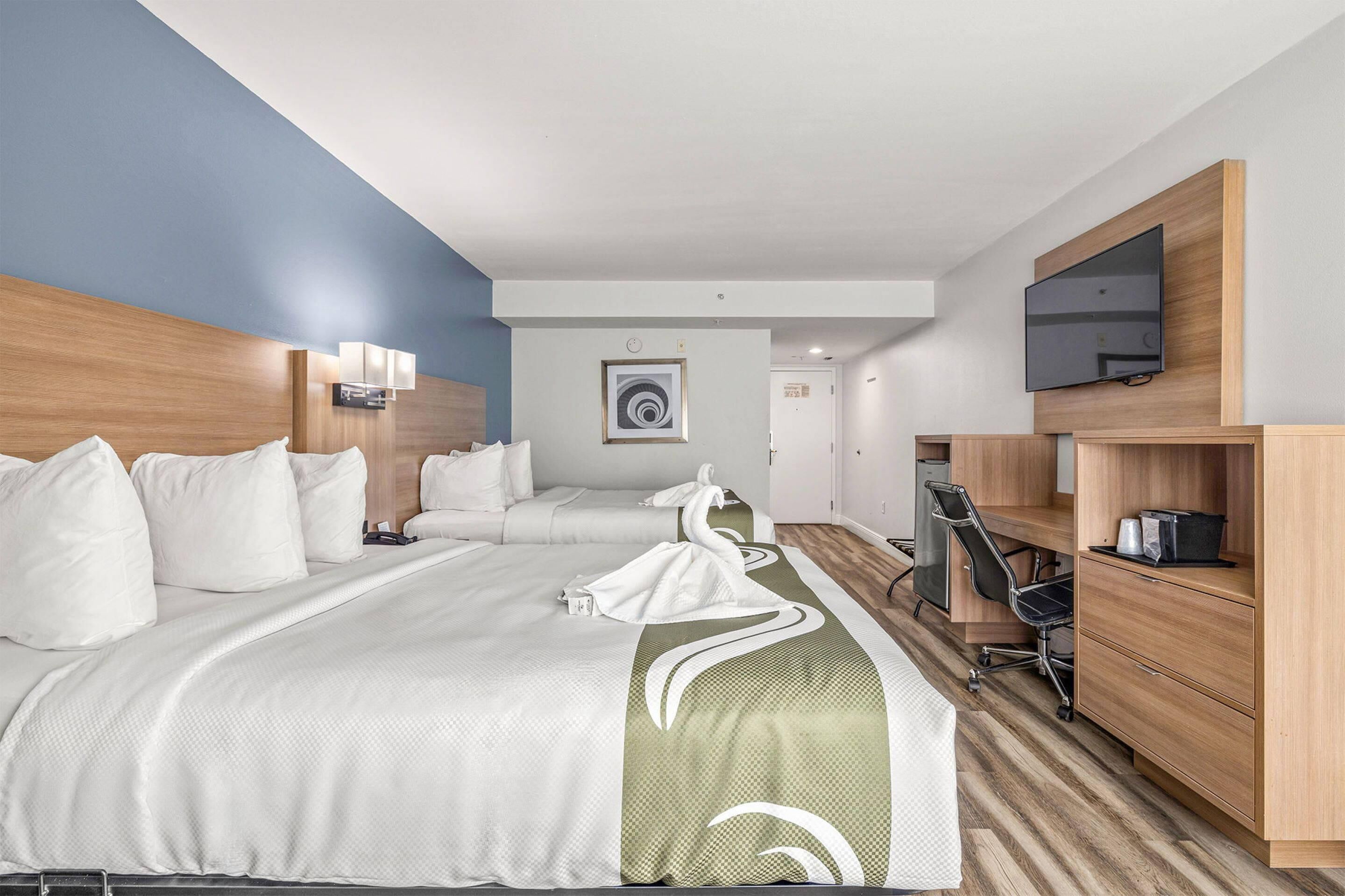 Een hotelkamer met twee bedden, een bureau, een stoel, een televisie en een zichtbare badkamer op de achtergrond.