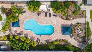 An aerial view of a swimming pool area with a curved pool, surrounded by lounge chairs, a barbecue area, and landscaped gardens. - Quality Inn & Suites Tampa near Fairgrounds and Casino (Tampa)