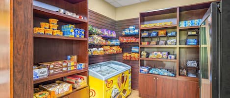 A corner of a store with shelves stocked with various snacks and boxed goods, a freezer, and wooden cabinets.