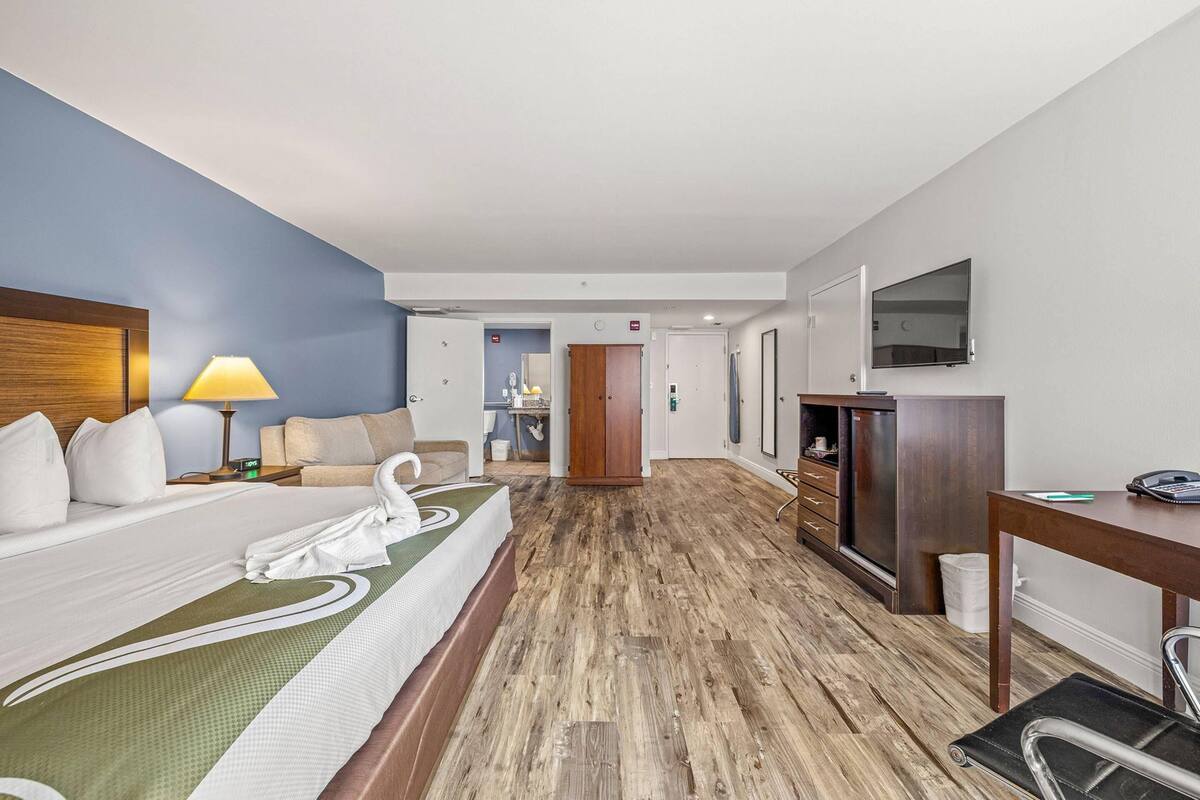 A hotel room with a bed, a desk, a chair, a television, and a bathroom visible through an open door.