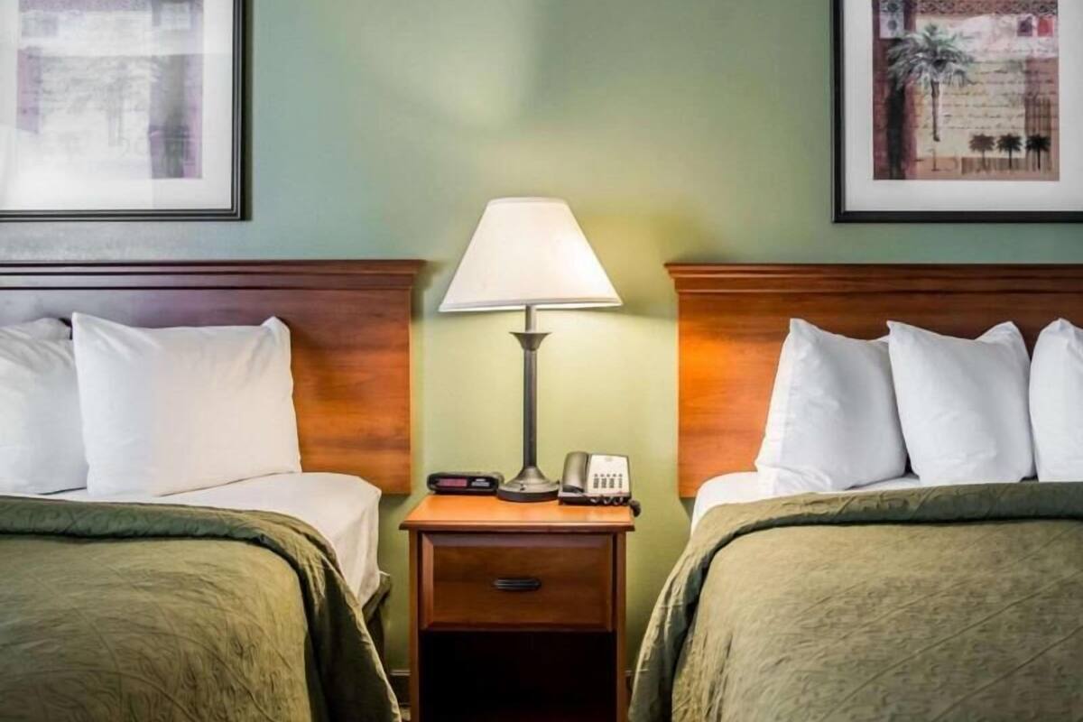 A hotel room with two beds, a nightstand with a lamp, and two framed pictures on the walls.