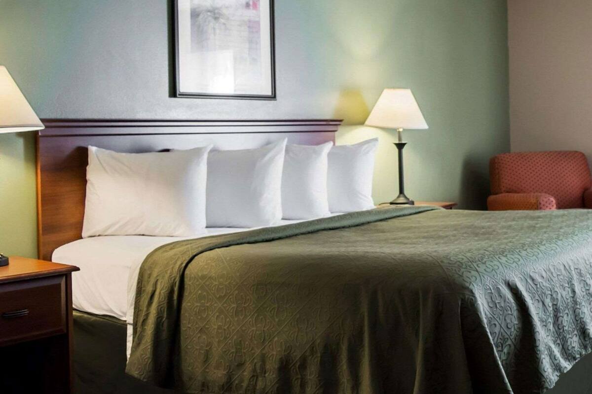 A hotel room with a bed, two bedside lamps, a framed picture on the wall, and a chair.