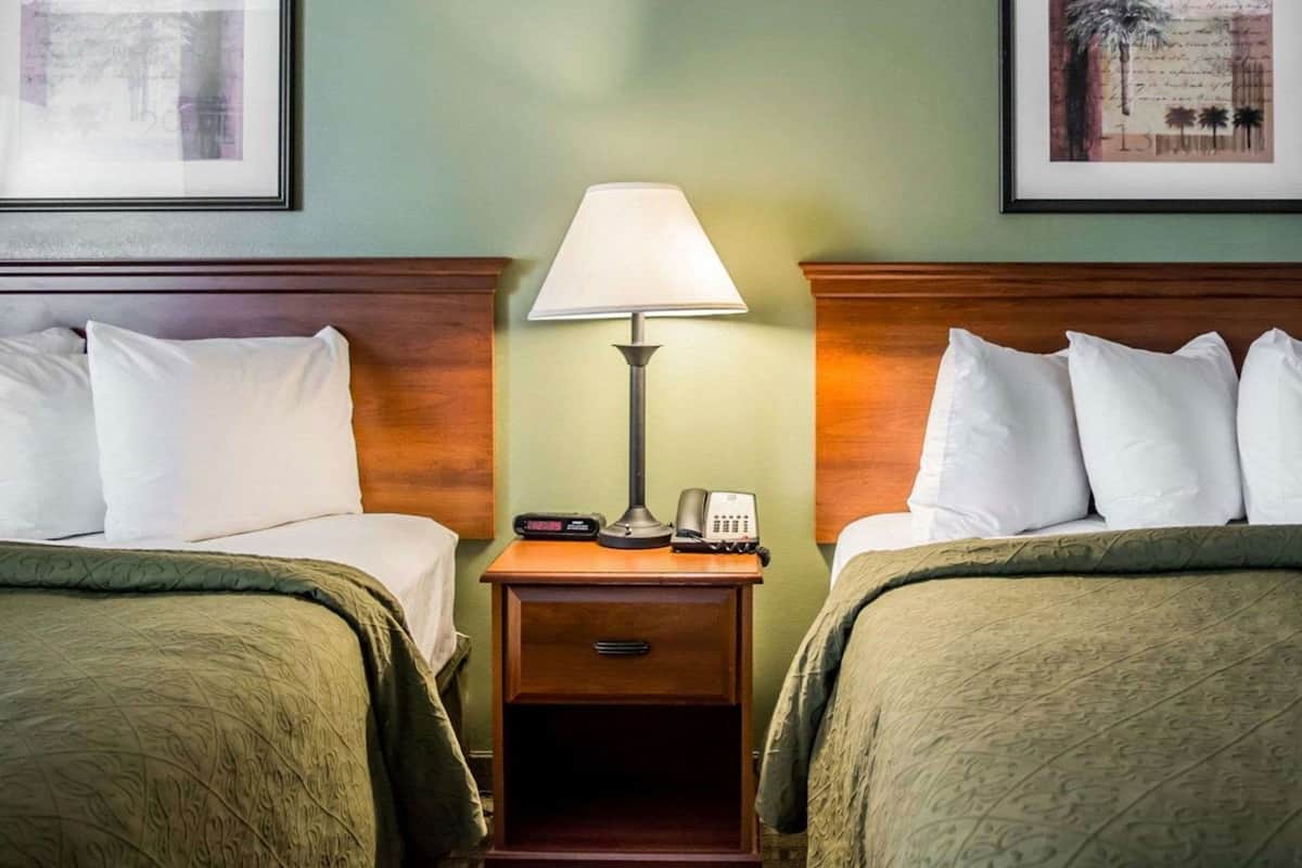 Ein Hotelzimmer mit zwei Betten, einem Nachttisch mit Lampe, einem Telefon und gerahmten Bildern an den Wänden.