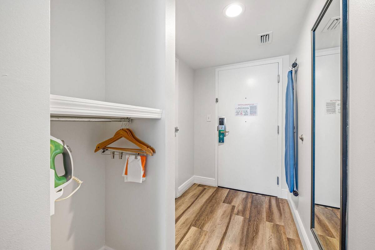 A hallway with a wooden floor, a white door with a blue towel hanging, and a coat rack with a green item and a wooden hanger.