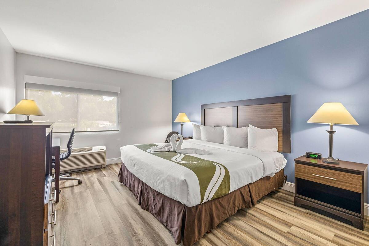 A hotel room with a bed, bedside lamps, a desk, and a window.